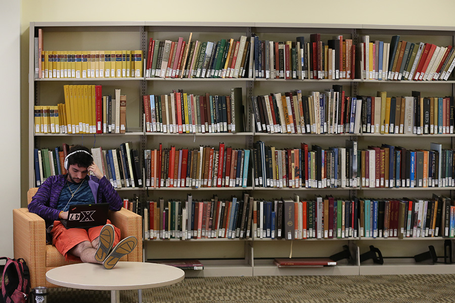A student sitting in the Xavier Library reading a book. There are bookshelves behind the student that are filled with books.
