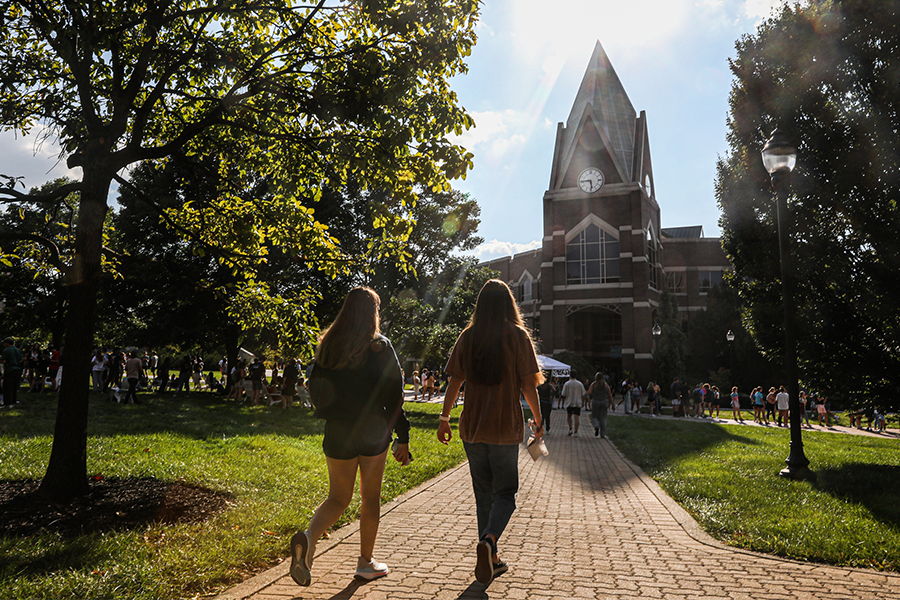 Two students walk together toward Gallagher Student Center, where there are lots of other students hanging out.