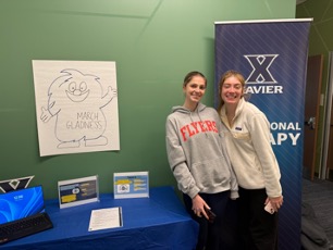 two students pose in front of march gladness booth