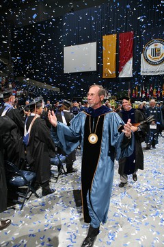 Father Graham walking through a graduating class during their graduation ceremony