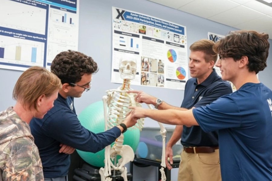 Three students and a professor look at a model human skeleton