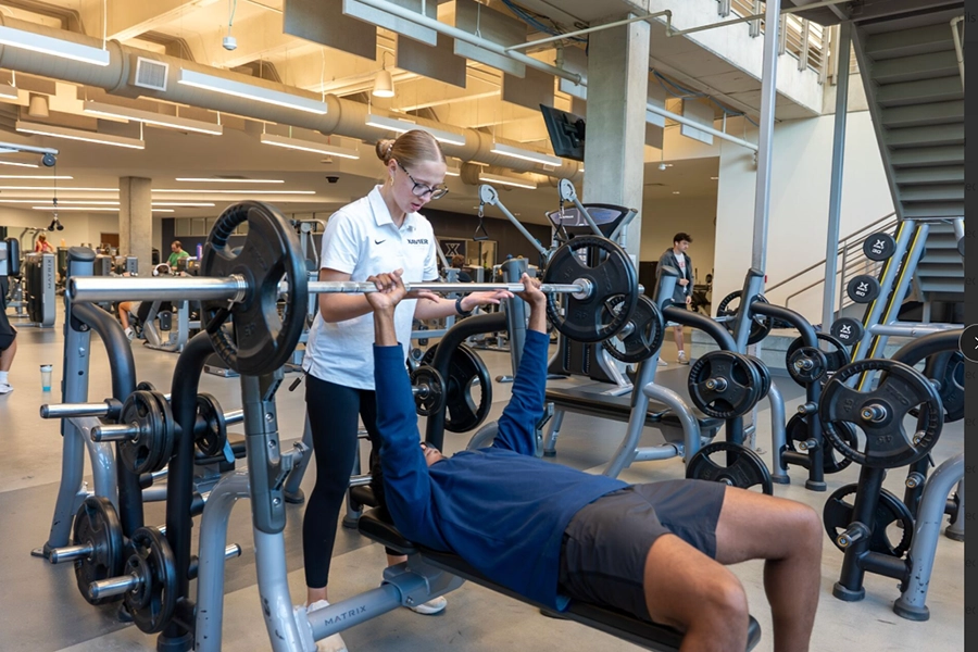 One student lifts weights while another student spots them