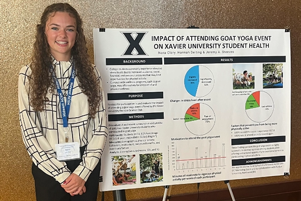 Nora standing in front of a research poster titled 'Impact of attending goat yoga on Xavier University student health'