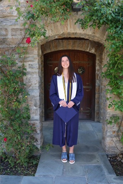 Maddy wearing a graduation gown outside of a chapel