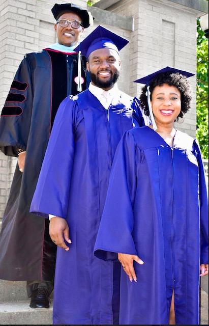 Two Xavier students in their graduation caps and gowns smiling with a Xavier professor, who is wearing commencement robes