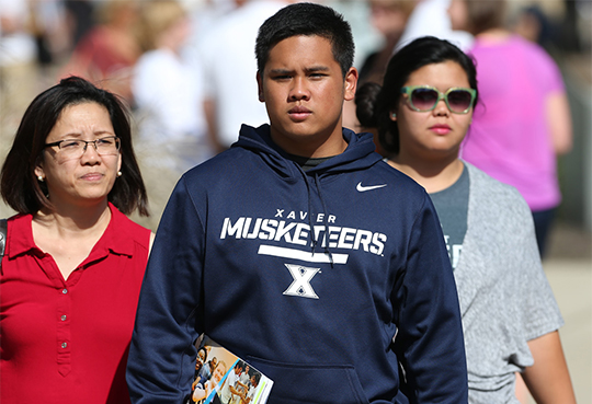 A student wearing a Xavier sweatshirt walking on campus with his family