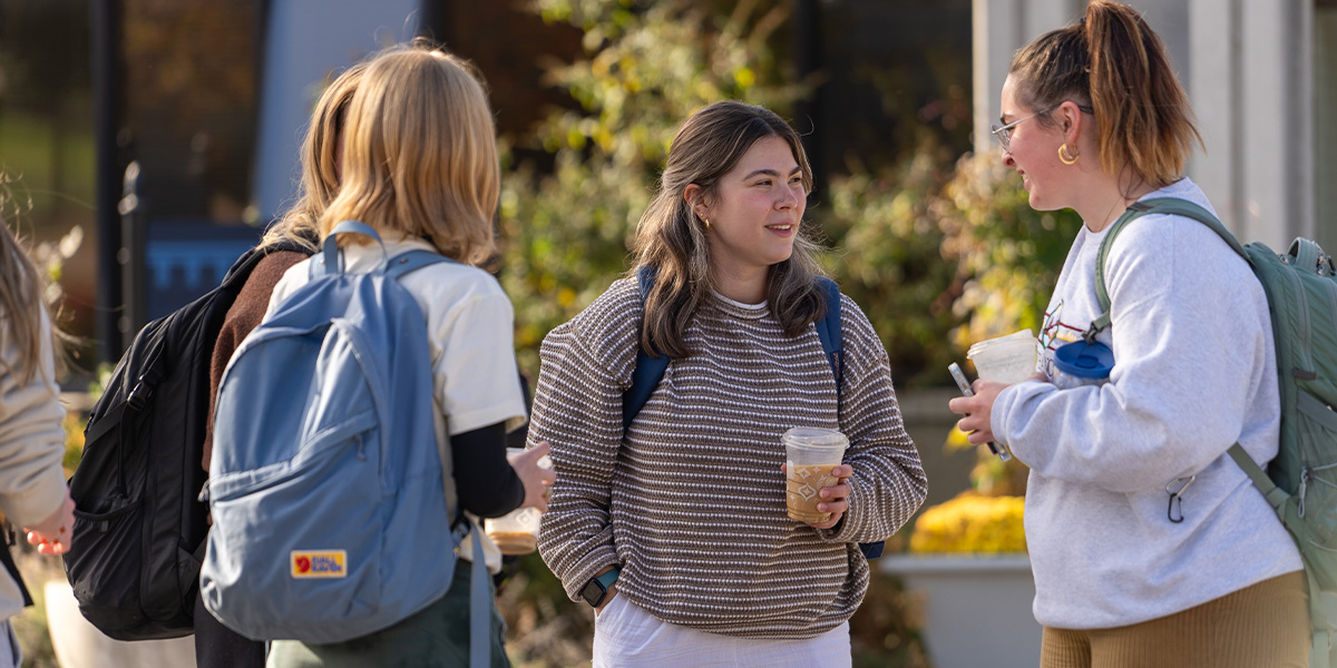 Students smiling on campus drinking coffee and talking