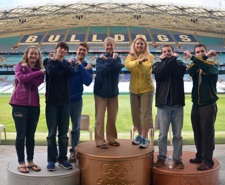 Photo of Students and Faculty members flashing the 'X' symbol in front of a Stadium in Australia