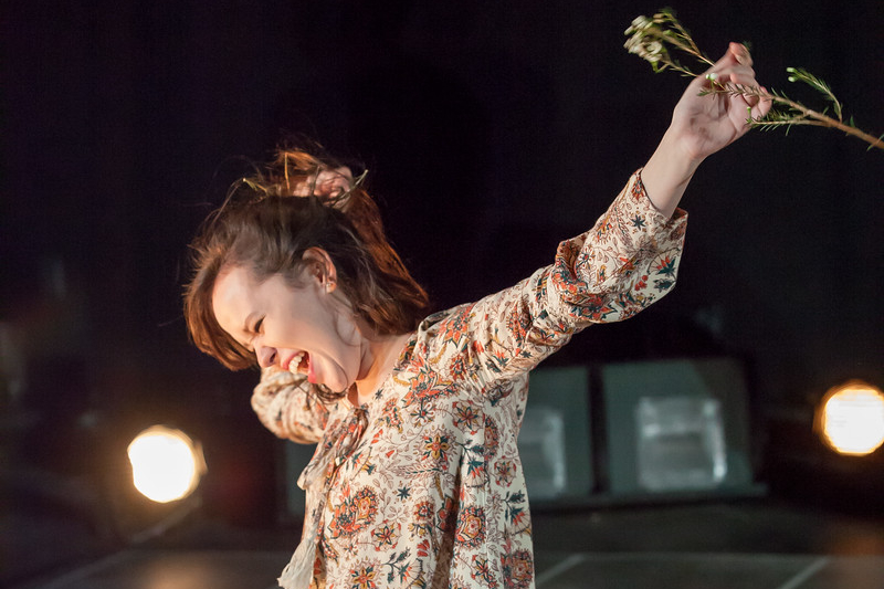 Actor on stage with their arms outstretched holding a flower