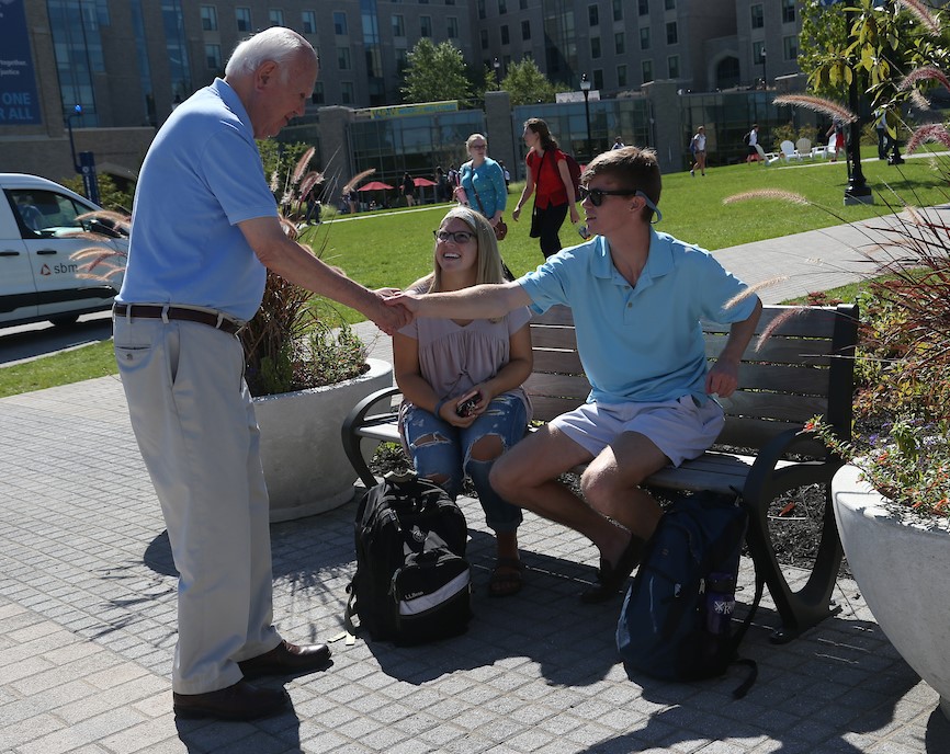 Father Bischoff shaking the hands of two students on Xavier's campus