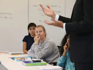 Two students sitting at desks listening to a speaker during a lecture