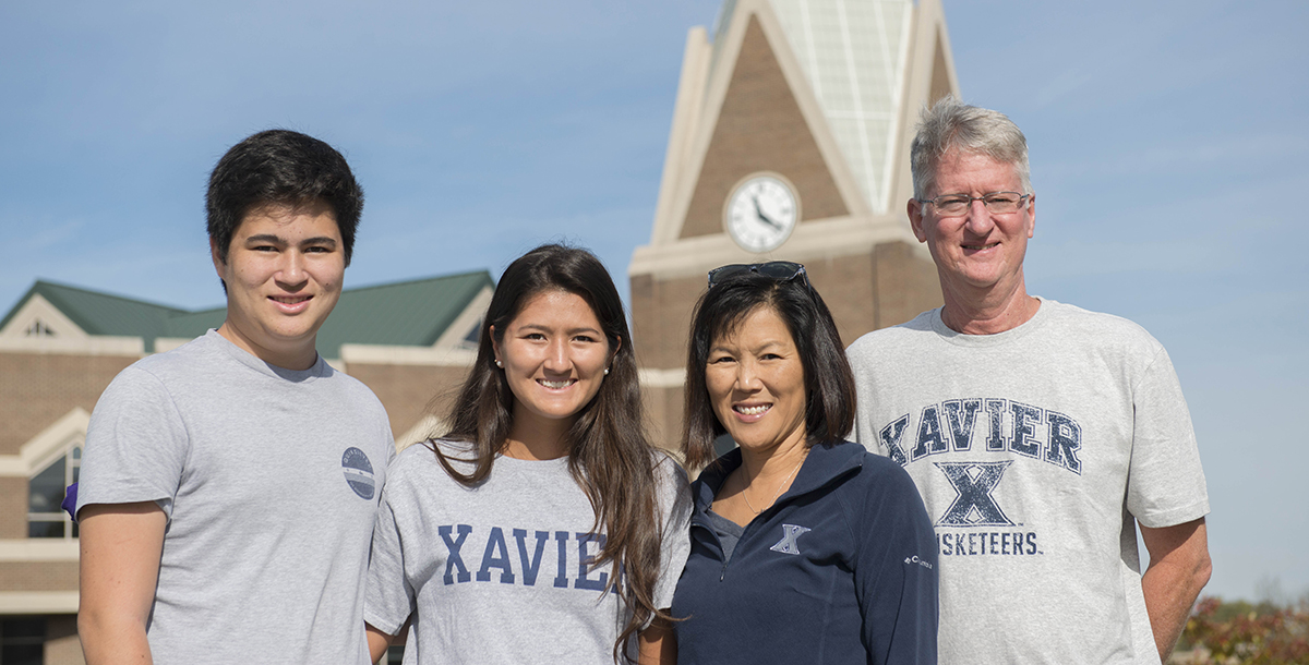 A family of four smiles in front of Gallagher Student Center on Xavier's campus.