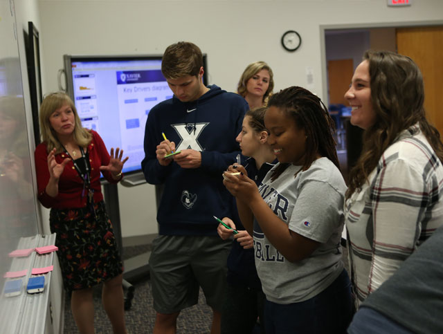 A group of Xavier students working on a whiteboard in a classroom