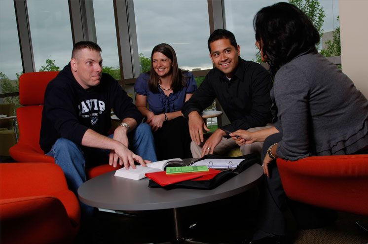 Four student sit on orange chairs in the Veteran and Military Family Center. They are smiling in conversation with each other.