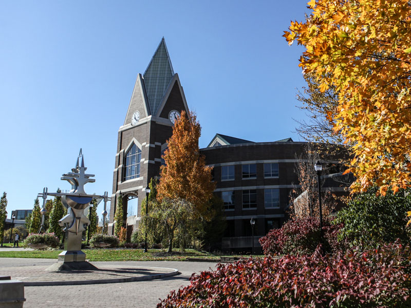 A photo of the exterior of Gallagher Student Center. There are two trees with orange leaves in front of the building. The sky is cloudless and blue.