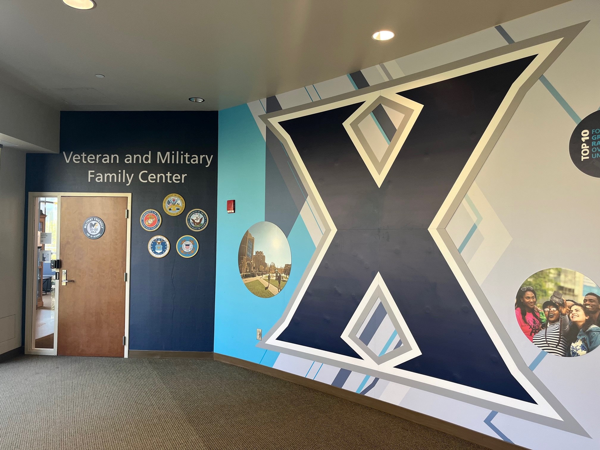 A photo of the interior of the Veteran and Family Military Center at Xavier. Two orange couches are visible. A large Xavier logo is hung on the wall behind the couches.