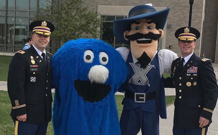 Two Xavier students in military uniform pose for a photo with Xavier's campus mascots, D'Artagnan and the Blue Blob.