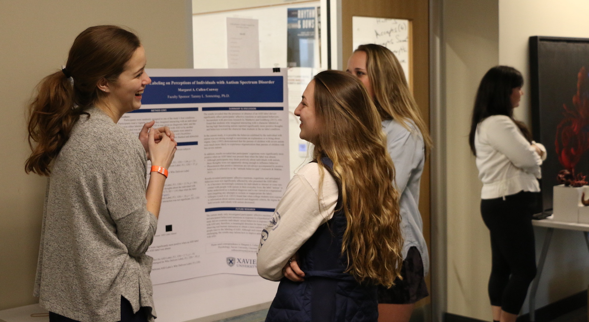Three students conversing in front of presentation board. 